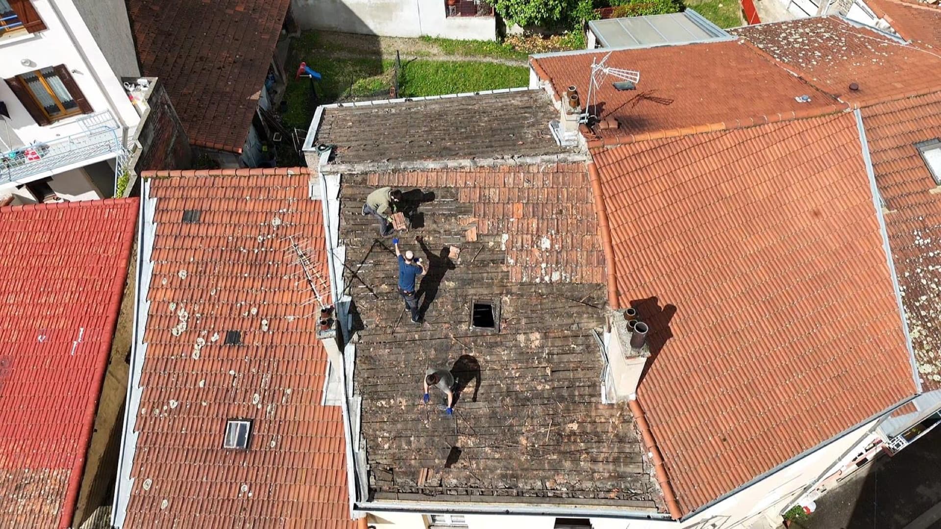 Trois couvreurs au travail sur une toiture en milieu urbain dense