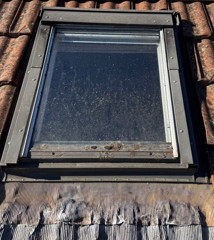 Ancienne fenêtre de toit au vitrage encrassé et à la bavette déformée